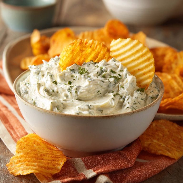 Cremiger Spinat-Kräuter-Dip als Nahaufnahme mit Kartoffelchips, die in die Schüssel gesteckt sind.