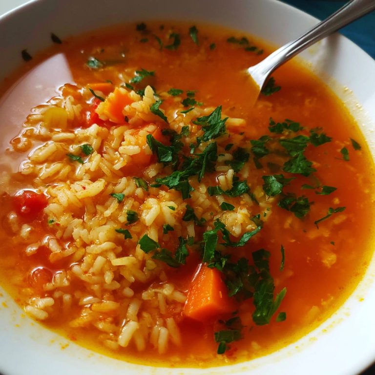 Reissuppe mit Gemüse als Nahaufnahme, garniert mit frischen Kräutern und Karottenstücken.