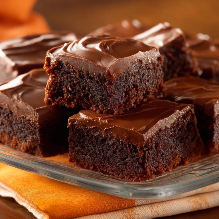 Saftige Schoko Brownies mit Glasur, gestapelt auf einer Glasplatte, mit einem Nahaufnahme-Fokus auf die glatte Schokoladenglasur und die dunkle Brownie-Textur.