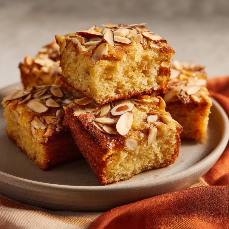 Saftiger Mandelkuchen vom Blech angeschnitten, mit einer Nahaufnahme der saftigen Krume und gerösteten Mandelblättchen.