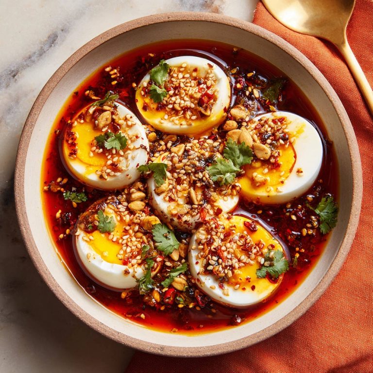 Würzige Eier in Chili-Öl als Nahaufnahme von oben in einer Schüssel mit Garnitur aus Sesam und Kräutern.