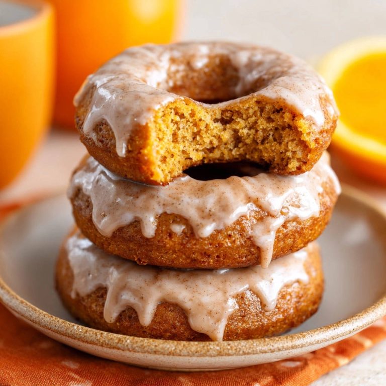 Kürbis-Donuts im Ofen gebacken, gestapelt auf einem Teller und angeschnitten, mit Glasur und Zimt verfeinert.