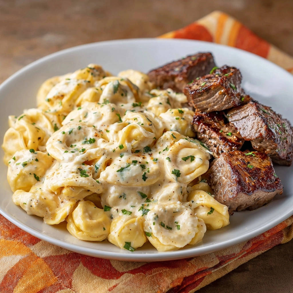 Saftige Rinderfilet-Würfel mit cremigen Tortellini, serviert auf einem weißen Teller mit Petersilie garniert.