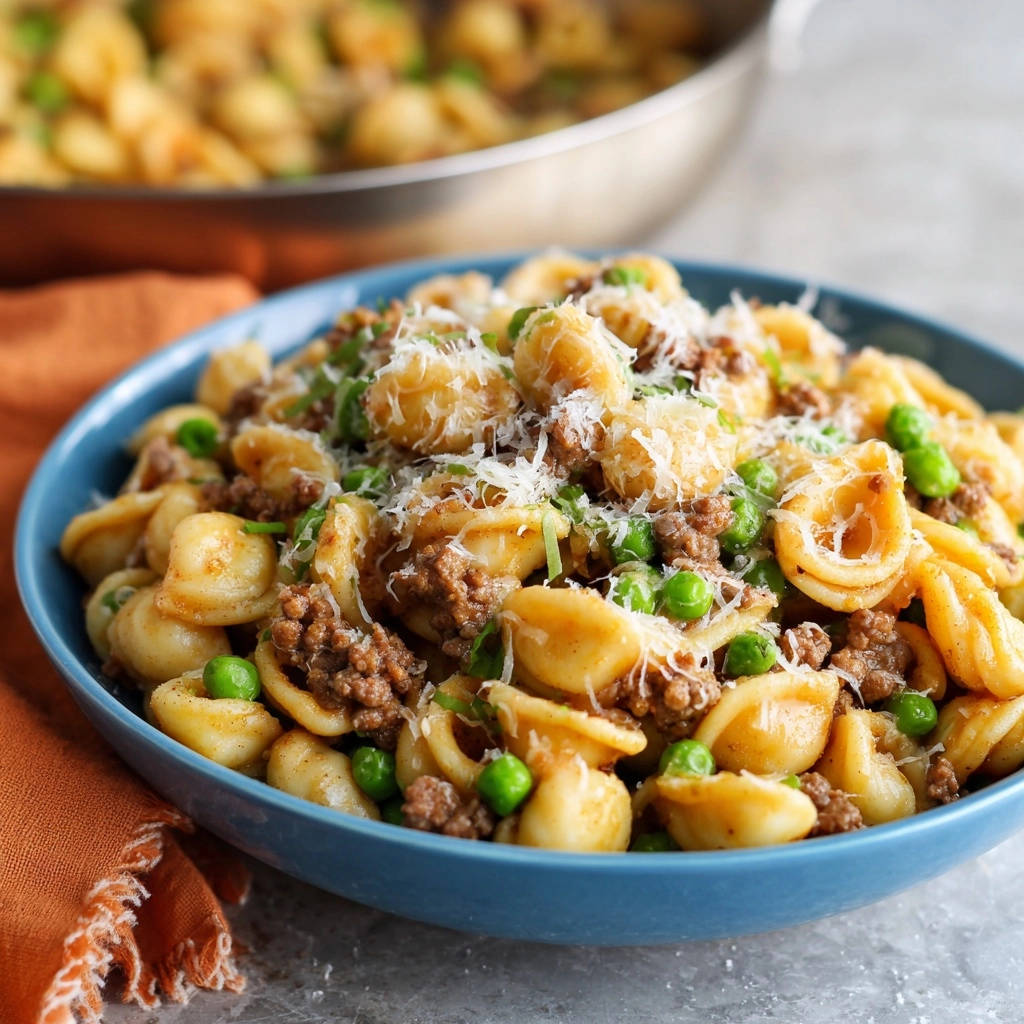 Herzhafte Orecchiette mit Hack und Erbsen, eine Nahaufnahme in einer blauen Schüssel, garniert mit geriebenem Parmesan.