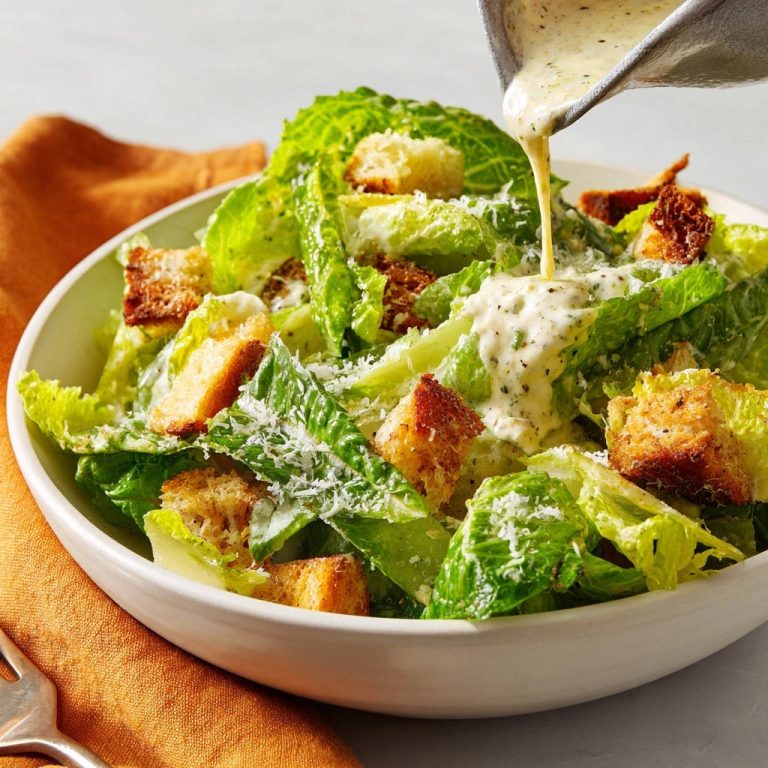 Klassischer Caesar Salat, bei dem cremiges Dressing über knackige Römersalatblätter und Croutons gegossen wird.
