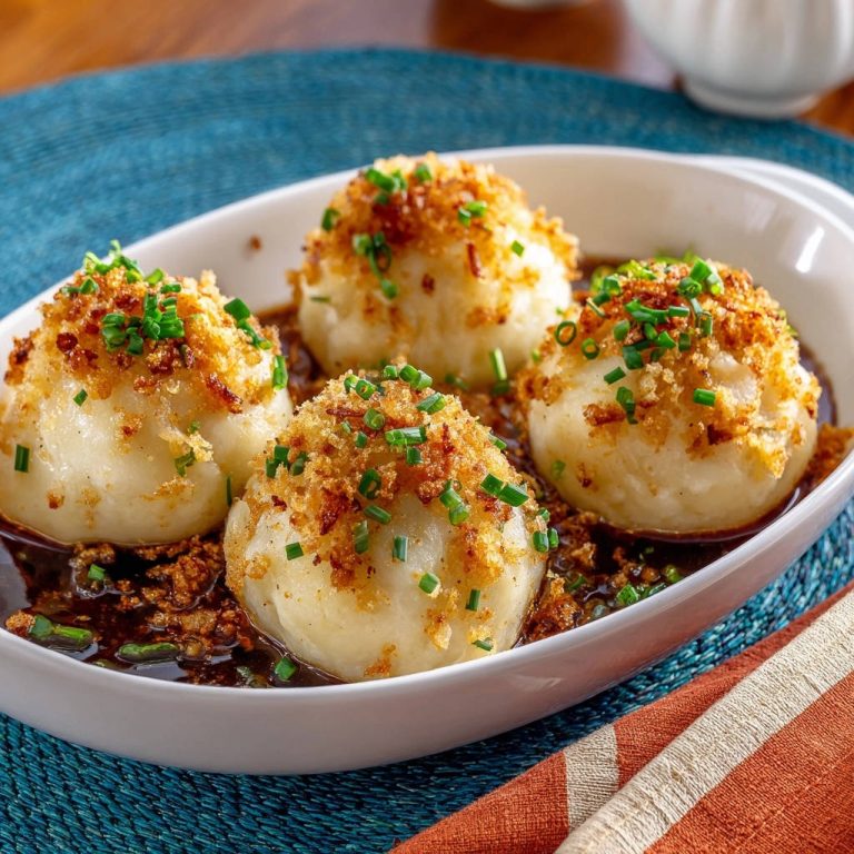 Herzhafte Kartoffelknödel in Bratensoße mit Butterbröseln, eine Nahaufnahme der Garnitur aus gebräunten Butterbröseln und Schnittlauch.