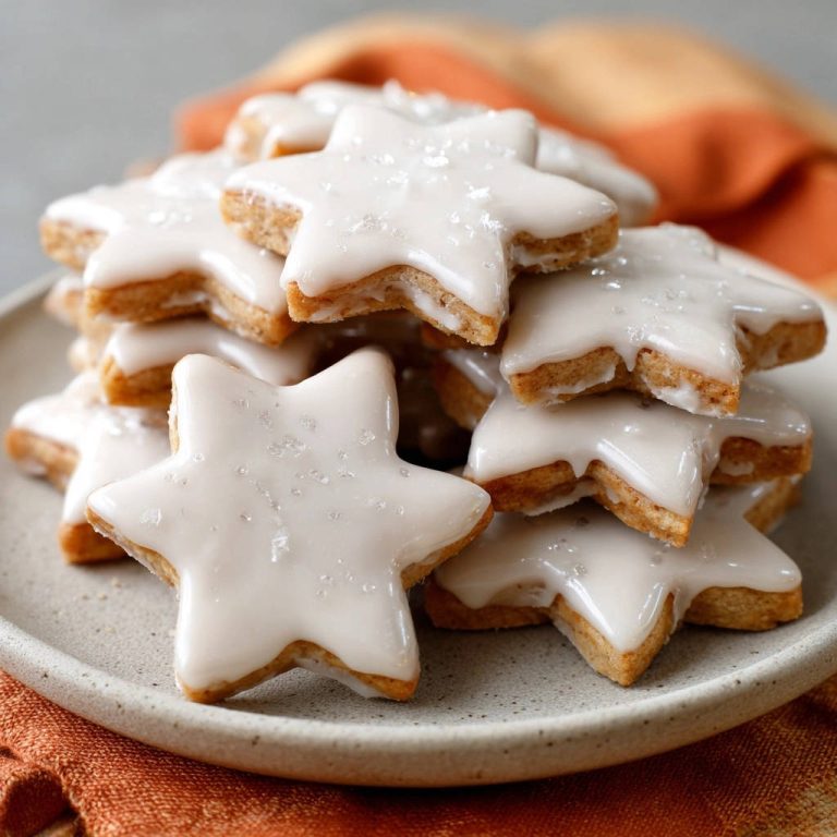 Mürbeteig-Sterne mit Zitronenguss, nahaufnahme der glasierten Sternenplätzchen auf einer Platte mit Zuckerkristallen