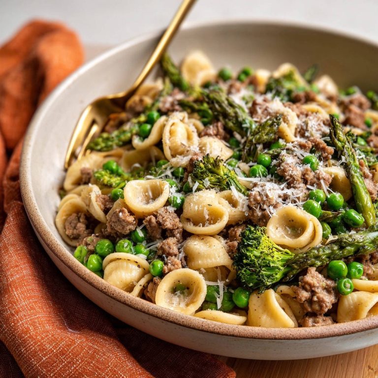 Orecchiette mit Hackfleisch und Frühlingsgemüse, nahaufnahme in einer Schüssel mit einem goldenen Löffel, garniert mit Parmesan.