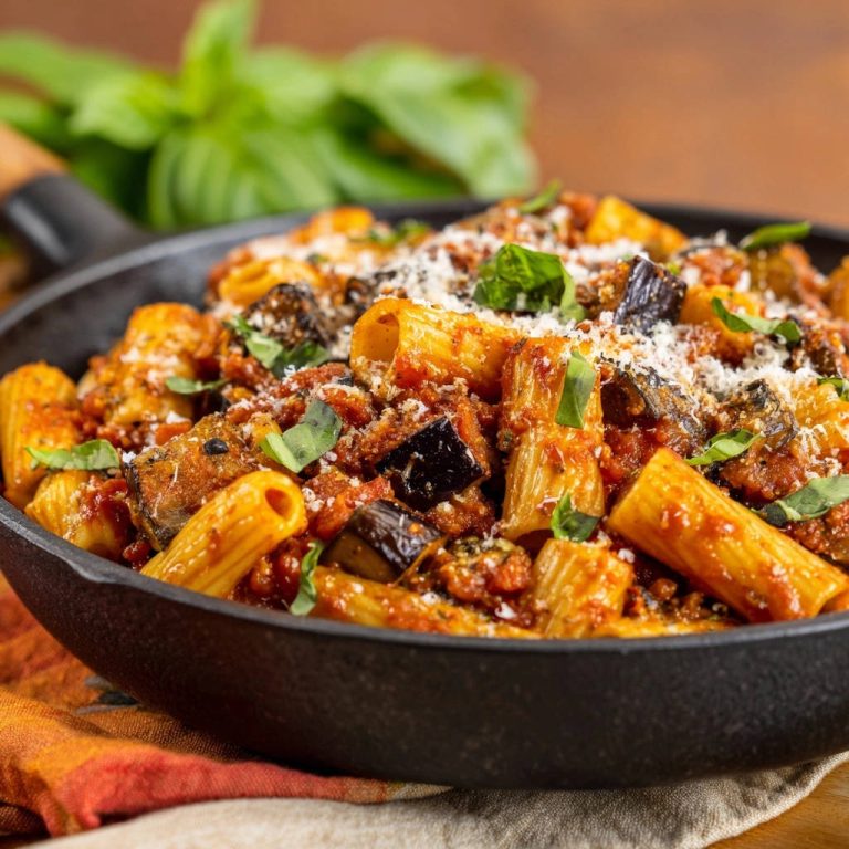 Rigatoni mit herzhaftem Auberginen-Ragu, Nahaufnahme des Gerichts in einer gusseisernen Pfanne mit Basilikum garniert.