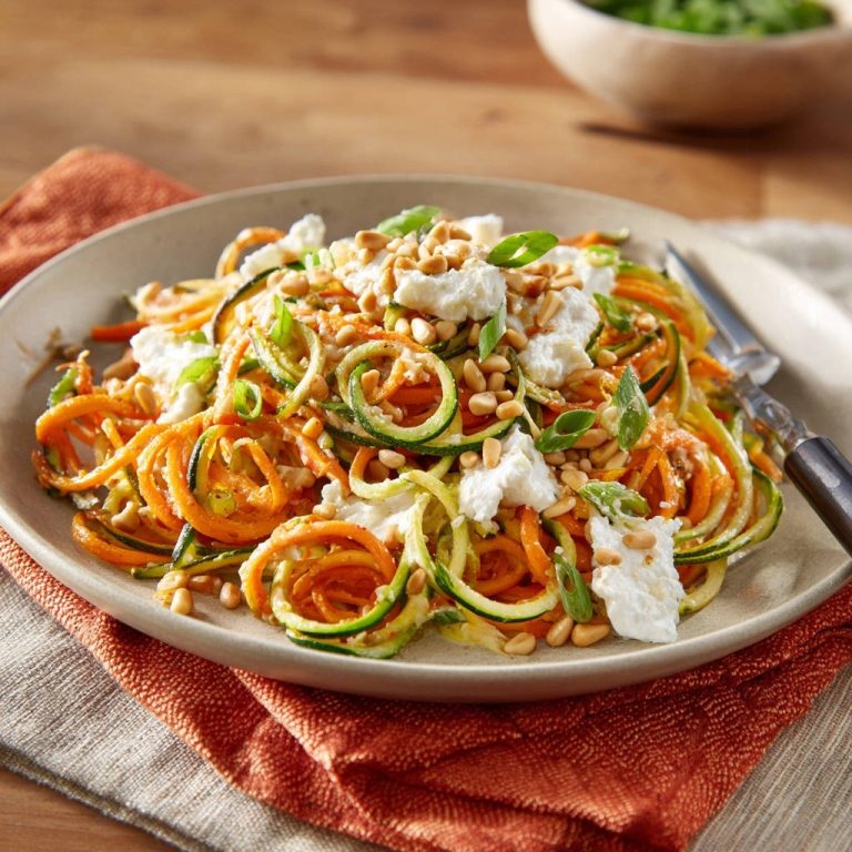 Frische Zucchini-Karotten-Spaghetti mit cremiger Note, garniert mit Ziegenkäse und Pinienkernen auf einem Teller