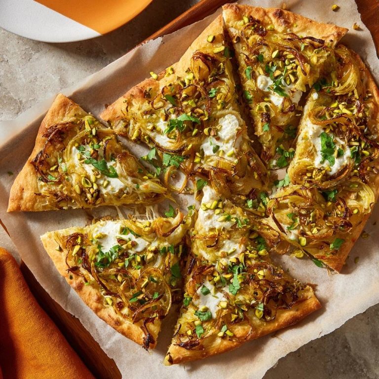 Knuspriger Zwiebel-Pistazien-Fladen mit Feta, angeschnitten und auf Backpapier liegend, mit gehackten Pistazien garniert.