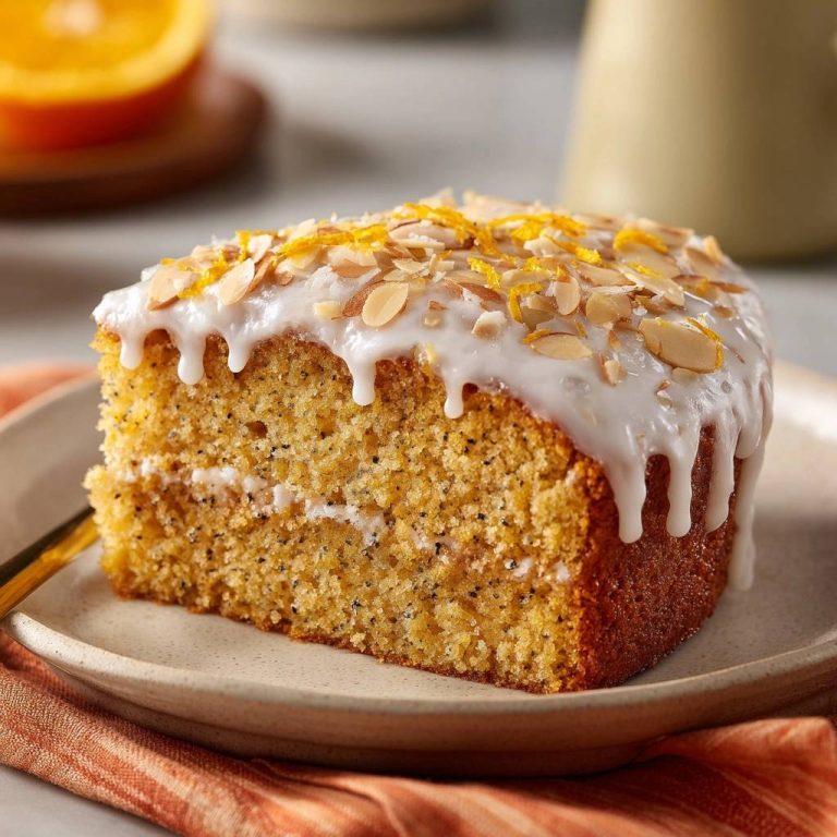Orangen-Mohnkuchen angeschnitten auf einem Teller, mit weißer Glasur und Mandelsplittern garniert