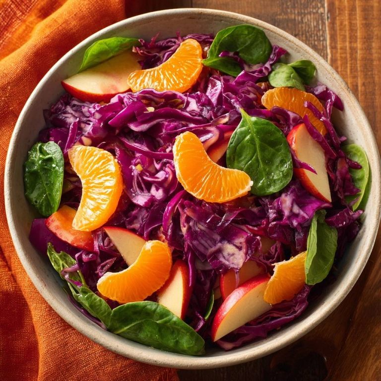 Orangiger Rotkohl-Spinat-Salat mit Apfelstücken und Mandarinen in einer Schüssel, detaillierte Draufsicht.