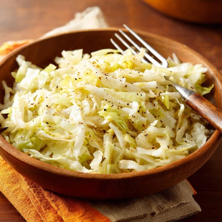 Zarter Weißkohl aus der Pfanne auf einer Gabel in einer Holzschale, mit schwarzem Pfeffer bestreut.