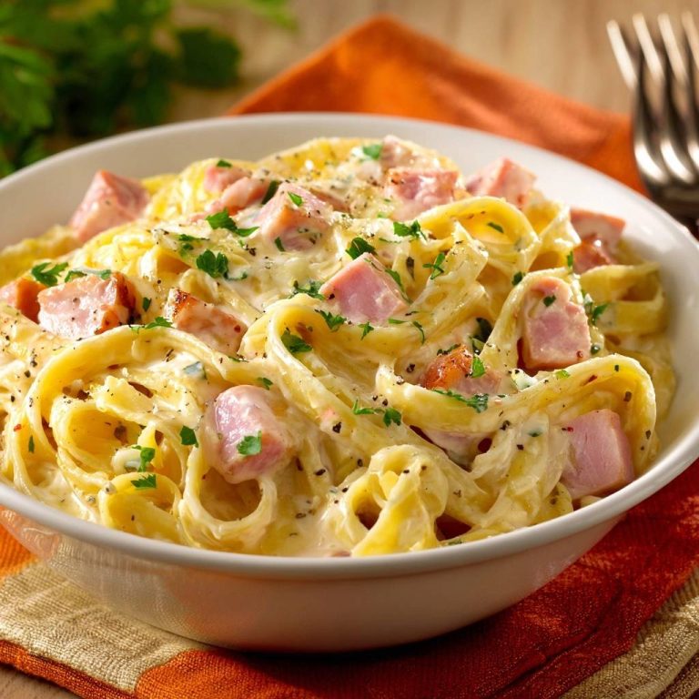 Cremige Tagliatelle mit Schinken in einer Schüssel, garniert mit Petersilie und schwarzem Pfeffer, detailreiche Nahaufnahme.